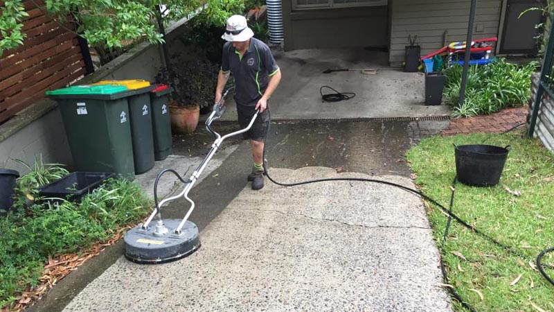 A Sydney Pressure Cleaning operator cleaning a driveway with a rotary surface cleaner.